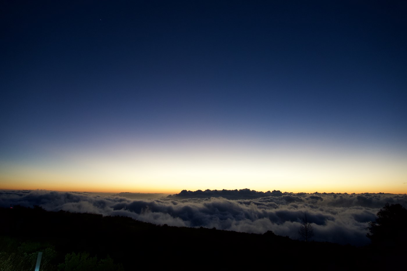 A band of orange light over a sea of clouds seen from high on a volcano in Maui