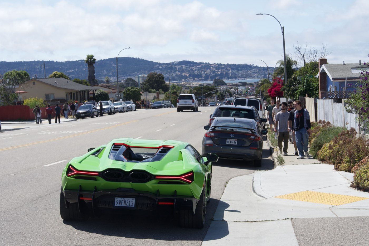 A green Lamborghini Revuelto seen from behind on a hillside street above Monterey Bay