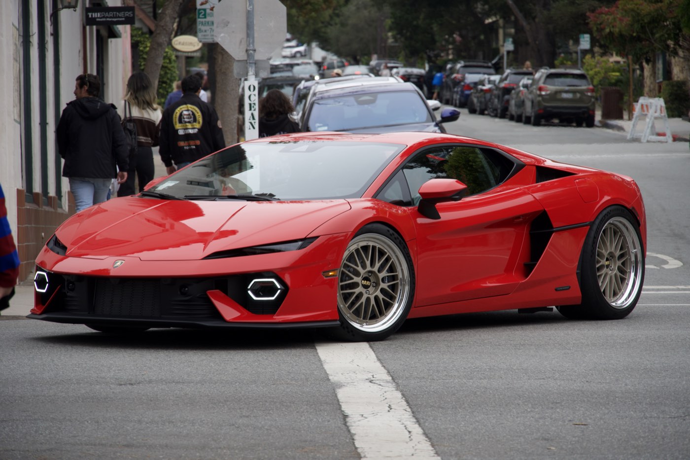 A red Lamborghini Temerario on gold wheels rolling down a street past onlookers