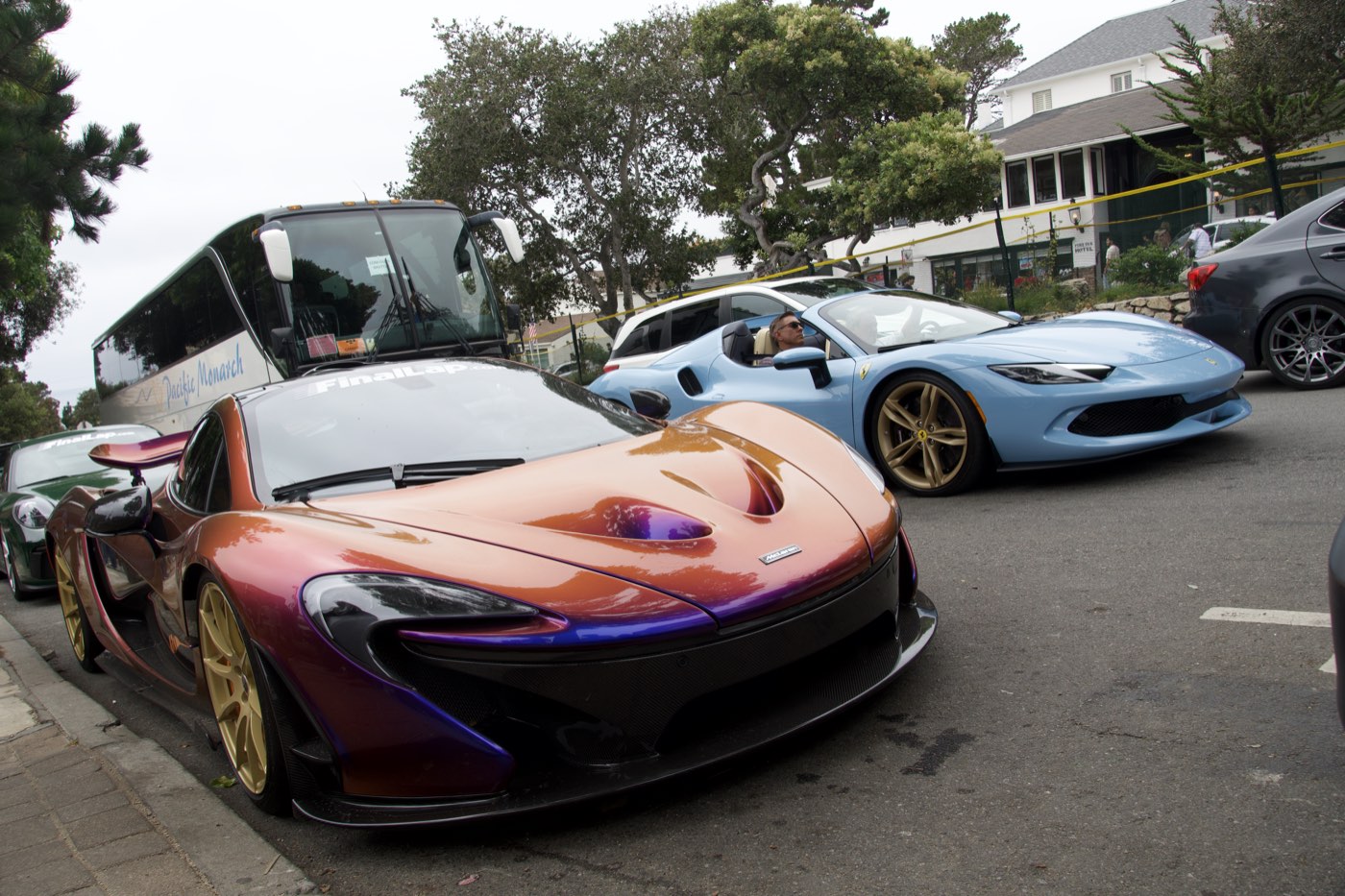 A colour-shifting McLaren P1 parked beside a light blue Ferrari 296 on a tree-lined street