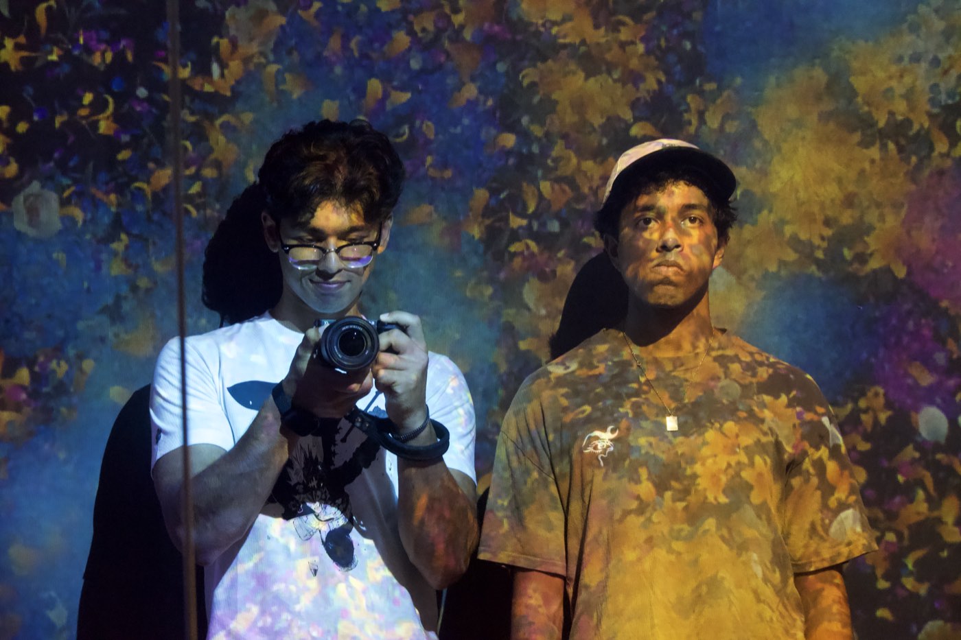 Shrish Choudhary holding a camera, lit by a projected floral installation at teamLab Borderless in Tokyo