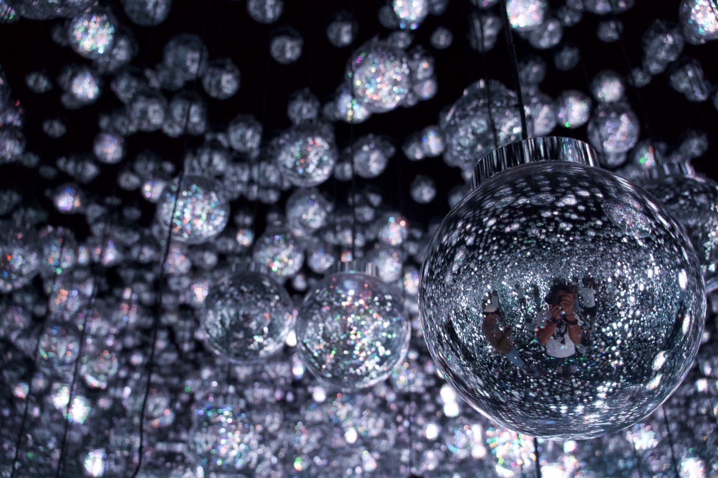 Suspended mirrored spheres filled with light at teamLab Borderless, a photographer reflected in the nearest one
