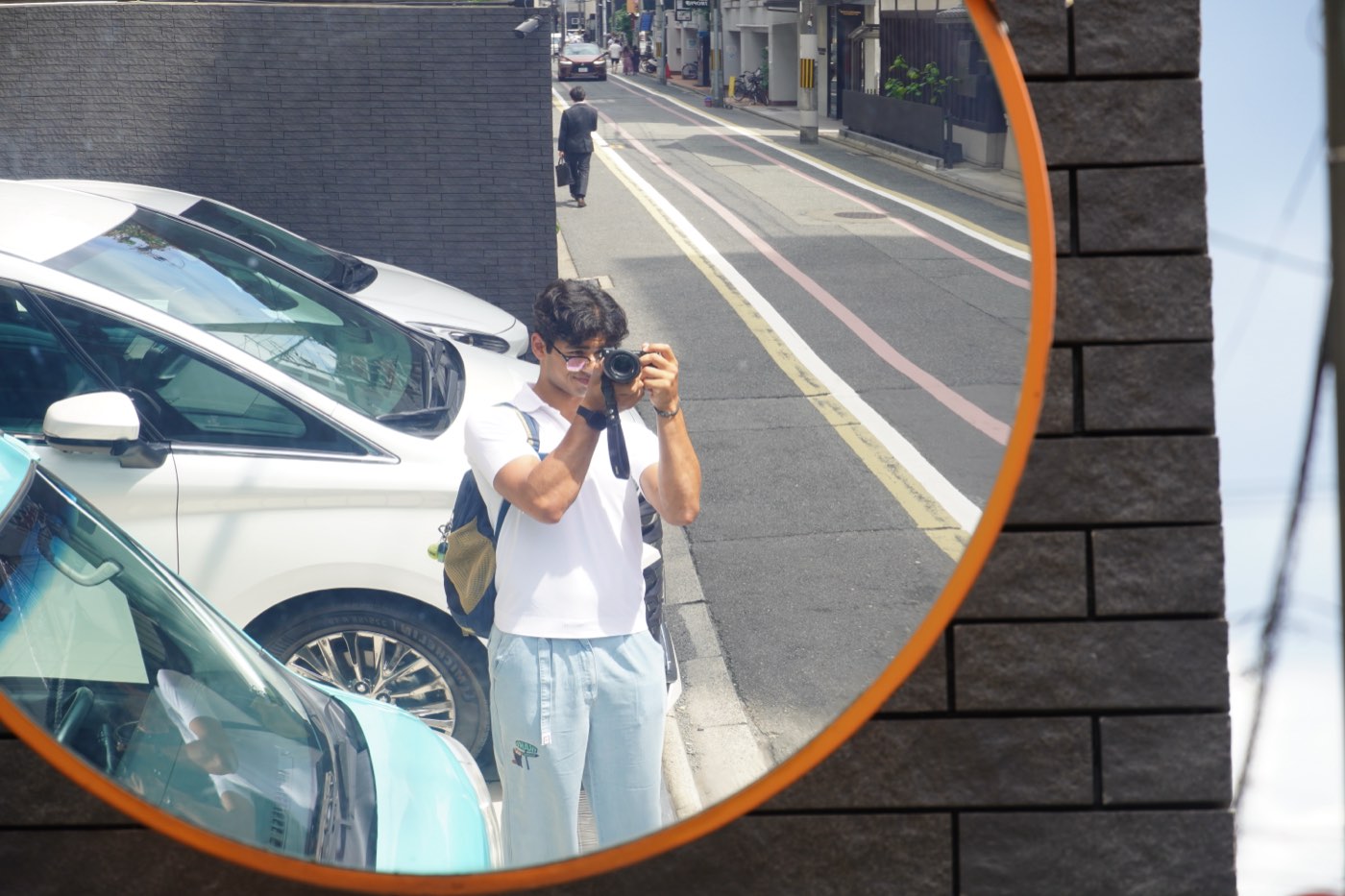 Shrish Choudhary photographed in the reflection of a round orange convex traffic mirror on a Kyoto street